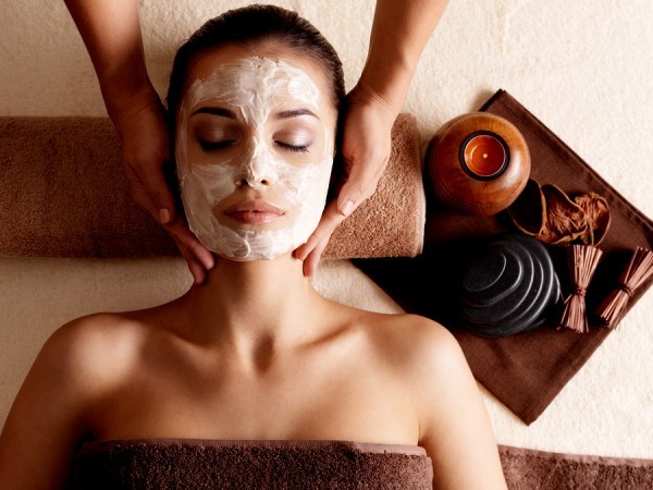 woman wearing a facial mask in spa setting. Esthetician gives facial massage.