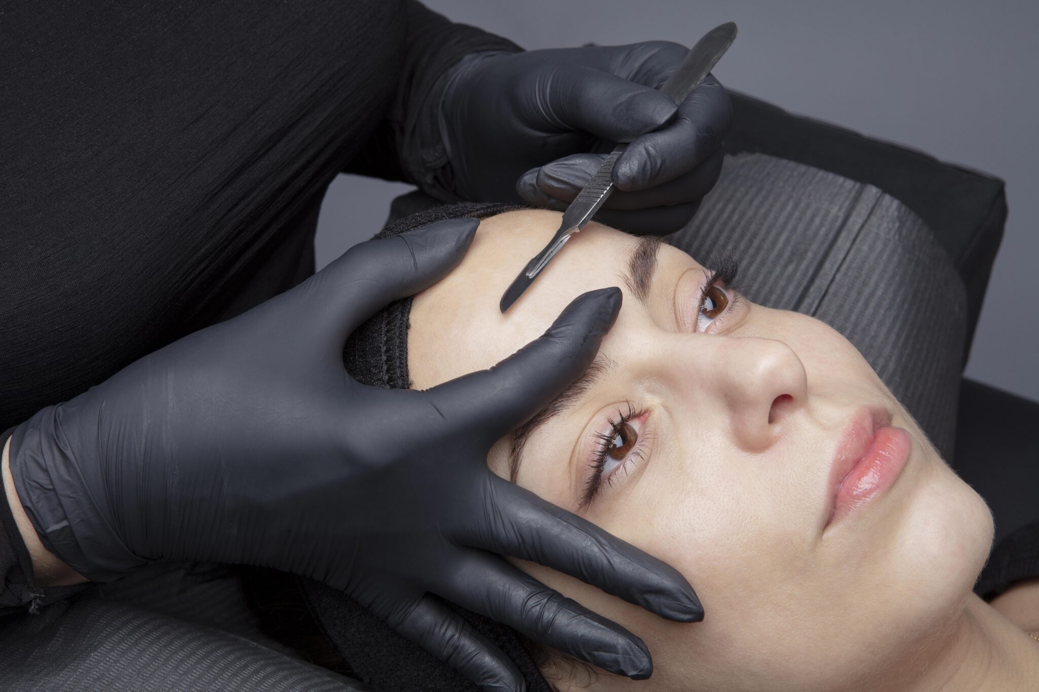 Close-up portrait of a woman in a salon, receiving a professional dermaplaning treatment from an esthetician