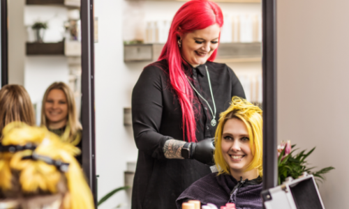 hairstylist with bright red hair applies color treatment to clients yellow hair